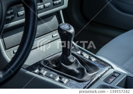A gear shift is visible inside a sports car in a modern showroom filled with vehicles during daylight A gear shift is visible inside a sports car in a modern showroom filled with vehicles during daylight 139557282