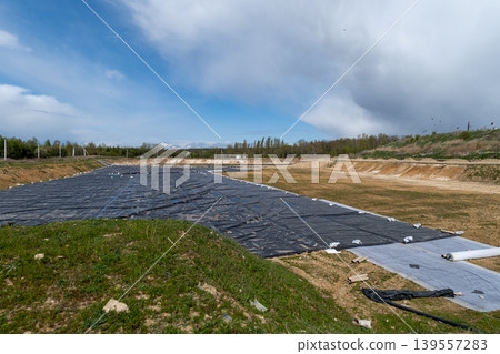 A large area at a municipal waste landfill is covered with black plastic for waste control in a rural setting with clear skies A large area at a municipal waste landfill is covered with black plastic for waste control in a rural setting with clear skies 139557283