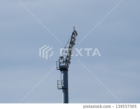 Side view of a high stadium lighting mast against a clear blue sky. 139557305