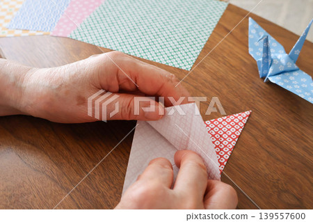 An elderly woman's hands folding origami on a table. An elderly woman's hands folding origami on a table. 139557600