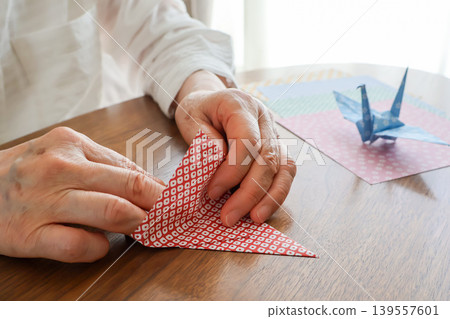 An elderly woman's hands folding origami on a table. 139557601