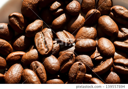 Close-up of roasted coffee beans with rich texture and natural sunlight. Macro background of brown aromatic coffee seeds. Concept of breakfast, energy, and cafe culture Close-up of roasted coffee beans with rich texture and natural sunlight. Macro background of brown aromatic coffee seeds. Concept of breakfast, energy, and cafe culture 139557894