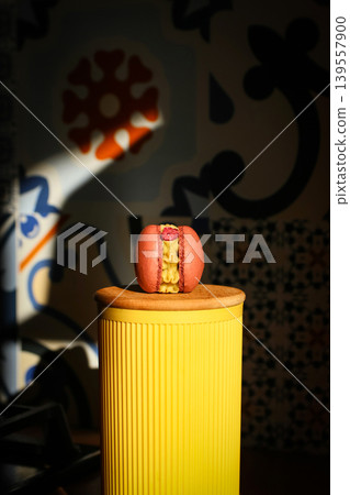 Close-up of a gourmet pink macaroon with yellow cream and raspberry on a yellow pedestal. French dessert with creative lighting on a decorative tile background 139557900