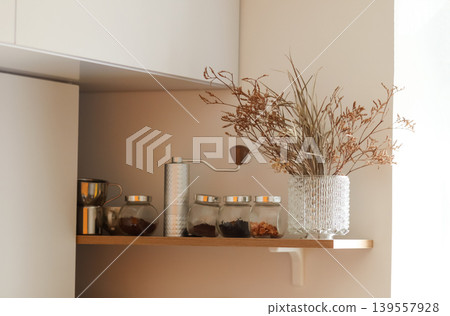 Modern kitchen shelf with manual coffee grinder, glass jars, and dried flowers in a vase. Minimalist interior design with cozy domestic atmosphere and copy space Modern kitchen shelf with manual coffee grinder, glass jars, and dried flowers in a vase. Minimalist interior design with cozy domestic atmosphere and copy space 139557928