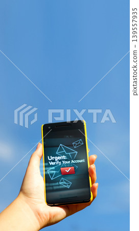 Hand holding a smartphone with an urgent account verification notification against a blue sky. Concept of cyber security, phishing alerts, and digital safety Hand holding a smartphone with an urgent account verification notification against a blue sky. Concept of cyber security, phishing alerts, and digital safety 139557935