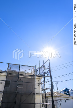 Exterior wall renovation site under a blue sky and sun: A detached house with ample open space. Exterior wall renovation site under a blue sky and sun: A detached house with ample open space. 139557981