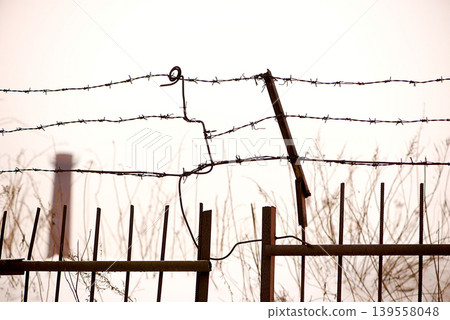 Broken Barbed Wire Fence Against Pale Sky Broken Barbed Wire Fence Against Pale Sky 139558048