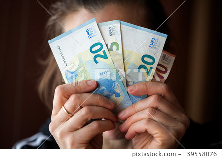 Person Hiding Face Behind Euro Banknotes Person Hiding Face Behind Euro Banknotes 139558076