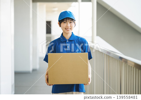 一位在快遞公司工作的年輕女子正在向一棟公寓大樓派送包裹。 一位在快遞公司工作的年輕女子正在向一棟公寓大樓派送包裹。 139558481