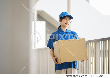 一位在快遞公司工作的年輕女子，正將包裹搬進公寓大樓。 139558483