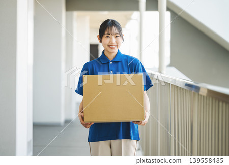 一位在快遞公司工作的年輕女子正在向一棟公寓大樓派送包裹。 一位在快遞公司工作的年輕女子正在向一棟公寓大樓派送包裹。 139558485