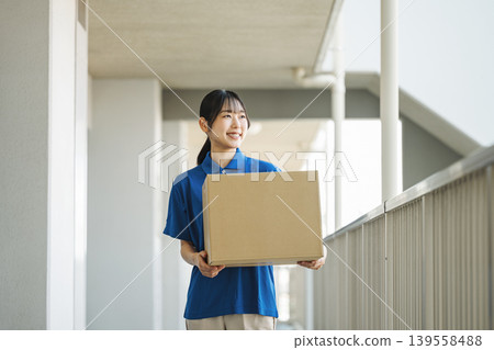 A young woman working for a delivery company delivers packages to an apartment building. A young woman working for a delivery company delivers packages to an apartment building. 139558488