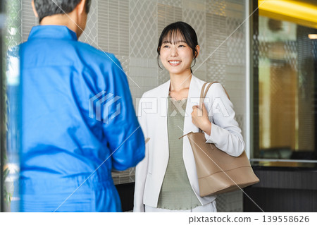 一位年輕女子在公寓大樓入口處與樓管交談。 139558626