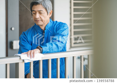 一位資深的男性建築管理員正在用抹布擦拭公寓大樓的欄桿。 一位資深的男性建築管理員正在用抹布擦拭公寓大樓的欄桿。 139558788