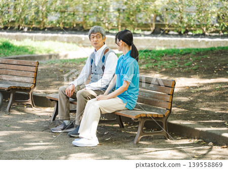 一位護理員和一位老年男性客戶坐在公園長椅上聊天。 139558869