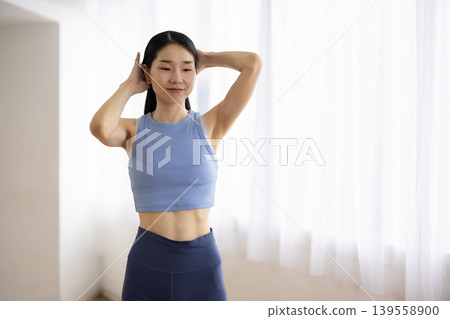 一位身穿瑜珈服的中年日本女性在明亮的窗邊紮起頭髮。 139558900