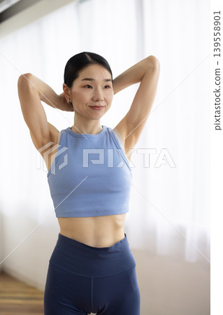 一位身穿瑜珈服的中年日本女性在明亮的窗邊紮起頭髮。 139558901