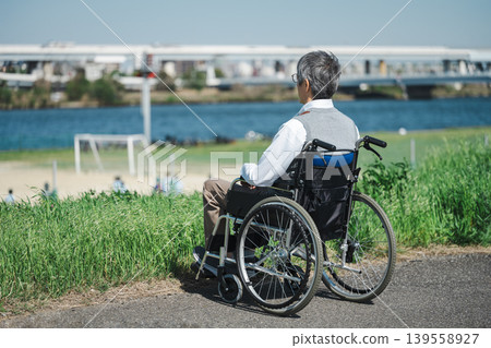 A senior man in a wheelchair relaxing on the riverbank. A senior man in a wheelchair relaxing on the riverbank. 139558927