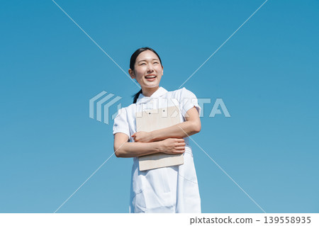 A young nurse standing against a blue sky. 139558935