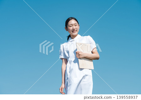 A young nurse standing against a blue sky. A young nurse standing against a blue sky. 139558937