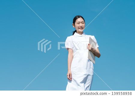 A young nurse standing against a blue sky. A young nurse standing against a blue sky. 139558938