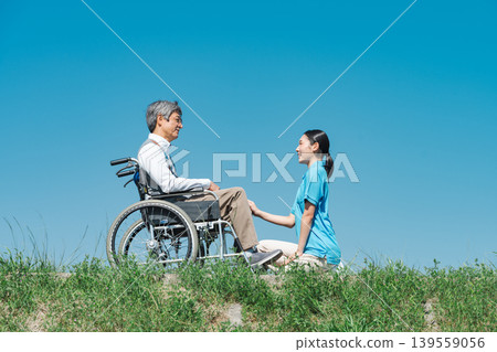 一位年輕的女護理員正在和一位坐在輪椅上的老人交談。 139559056