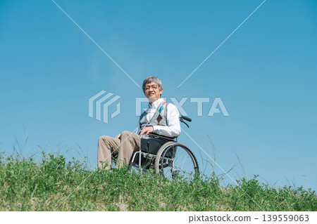 A senior man in a wheelchair strolls along the riverbank. A senior man in a wheelchair strolls along the riverbank. 139559063