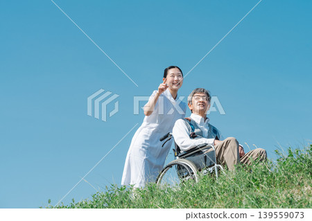 A nurse in a white coat and a senior man walking in a wheelchair A nurse in a white coat and a senior man walking in a wheelchair 139559073