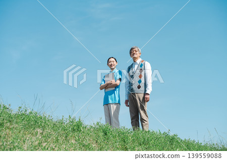 A caregiver and a senior man walking together along the riverbank 139559088