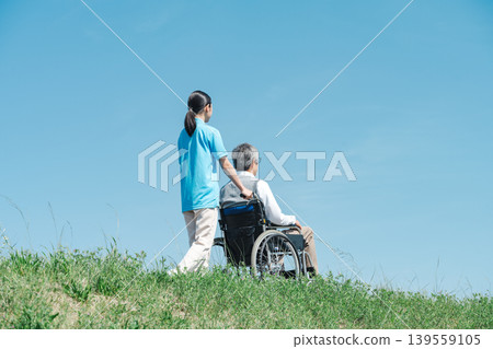 一位護理人員和一位坐在輪椅上的老人沿著河岸散步。 一位護理人員和一位坐在輪椅上的老人沿著河岸散步。 139559105