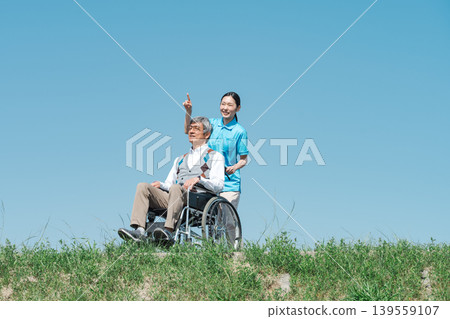 一位護理人員和一位坐在輪椅上的老人沿著河岸散步。 一位護理人員和一位坐在輪椅上的老人沿著河岸散步。 139559107