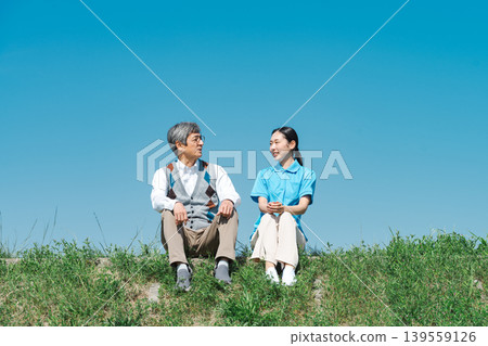 A caregiver and a senior man sitting and talking on the riverbank A caregiver and a senior man sitting and talking on the riverbank 139559126