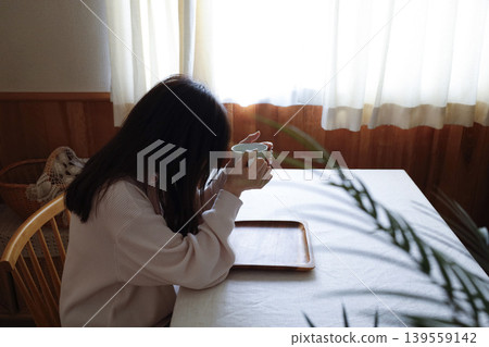 A woman in her loungewear, with her hair unstyled, drinks hot water – an image of slowly getting into the rhythm of the morning. 139559142