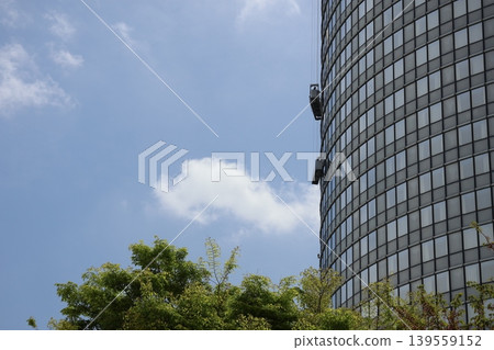 A landscape of green trees, white clouds, a blue sky, and a skyscraper with two window-cleaning gondolas. A landscape of green trees, white clouds, a blue sky, and a skyscraper with two window-cleaning gondolas. 139559152