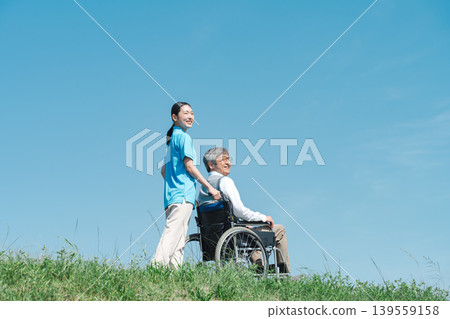 一位護理人員和一位坐在輪椅上的老人在公園散步。 一位護理人員和一位坐在輪椅上的老人在公園散步。 139559158