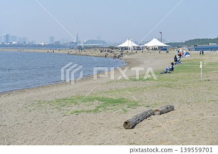 A bustling beach park by the sea; people spend their early summer holidays as they please on the sandy beach lined with tents. A bustling beach park by the sea; people spend their early summer holidays as they please on the sandy beach lined with tents. 139559701