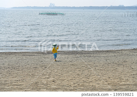 A child walks towards the vast ocean; a tranquil beach scene that fosters curiosity and a sense of adventure for the future. A child walks towards the vast ocean; a tranquil beach scene that fosters curiosity and a sense of adventure for the future. 139559821