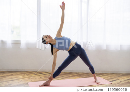 一位日本女子在明亮的窗戶旁的墊子上練習半月式（Ardha Chandrasana）。 139560056