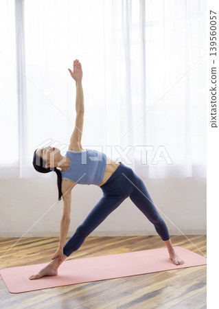 一位日本女子在明亮的窗戶旁的墊子上練習半月式（Ardha Chandrasana）。 139560057