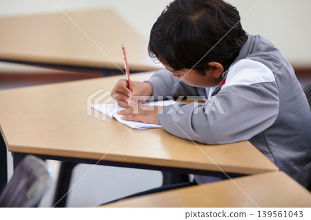 Boy, school and writing in classroom with notebook, studying lesson and learning knowledge at desk. Child, student and kid drawing on paper for academic development, educational test and assessment Boy, school and writing in classroom with notebook, studying lesson and learning knowledge at desk. Child, student and kid drawing on paper for academic development, educational test and assessment 139561043