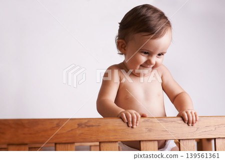 Happy baby in crib, playing with smile and fun in home, child development and care in house. Toddler girl in cot with playful face, energy and curiosity in cute kids bedroom, nursery or apartment. 139561361