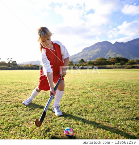 Girl, green grass and playing hockey for game, outdoor match or sports in nature for practice. Female person, kid or playful child enjoying competition with ball on field for fitness or training 139562259