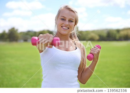 Happy woman, portrait and dumbbells for outdoor exercise, workout or training in nature. Face of young active female person or blonde smile for weightlifting, health and wellness on green grass field Happy woman, portrait and dumbbells for outdoor exercise, workout or training in nature. Face of young active female person or blonde smile for weightlifting, health and wellness on green grass field 139562336