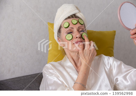 Woman enjoying a relaxing facial treatment with cucumber slices at home in the evening Woman enjoying a relaxing facial treatment with cucumber slices at home in the evening 139562998