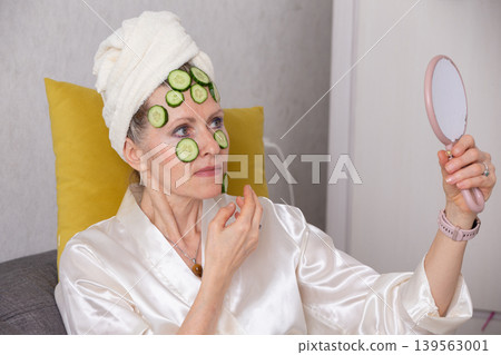 Relaxing spa day at home for a mature woman enjoying cucumber treatment while looking in the mirror Relaxing spa day at home for a mature woman enjoying cucumber treatment while looking in the mirror 139563001
