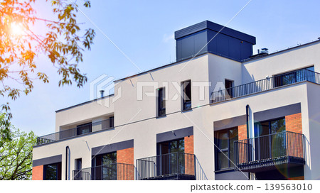 Architecture and real estate, residential apartment building with large panoramic windows. Modern building surrounded by nature, park, green trees, and blue sky background. Architecture and real estate, residential apartment building with large panoramic windows. Modern building surrounded by nature, park, green trees, and blue sky background. 139563010