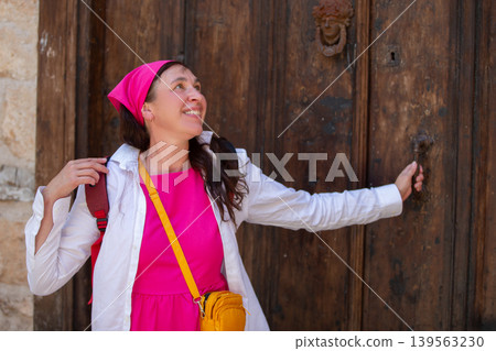 Woman in bright pink dress smiles while reaching for an ornate door handle in a historic location Woman in bright pink dress smiles while reaching for an ornate door handle in a historic location 139563230