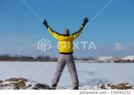 Person enjoys a winter day with raised arms in a snowy landscape under a blue sky Person enjoys a winter day with raised arms in a snowy landscape under a blue sky 139563232
