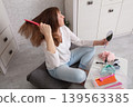 Woman styling her hair at home while sitting on a soft cushion 139563385