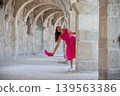 A female traveler looks out from the ancient columns and waves a scarf. She is wearing pink clothes. 139563386